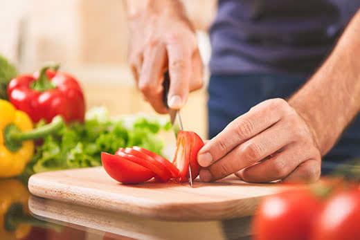 cucina, cibo e concetto di casa: primo piano di mani maschili che tagliano pomodori su un tagliere a casa