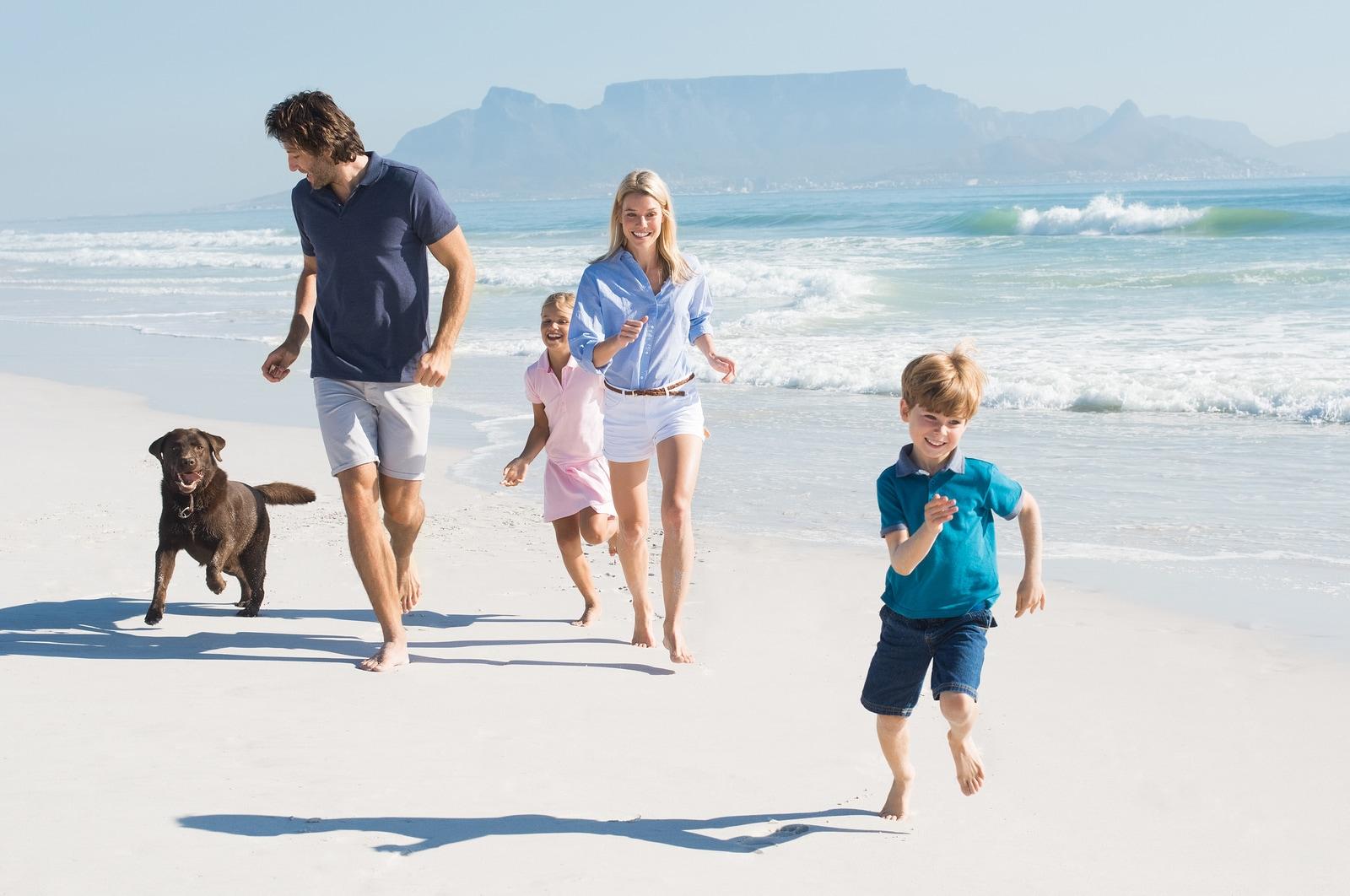 Family with two small children and brown dog running on the beach.